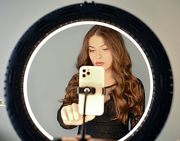 Junge Frau filmt sich selbst mit einem Handy und Ringlicht Junge Frau filmt sich selbst mit einem Handy und Ringlicht