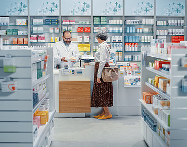 Frau steht an der Theke und redet mit dem Apotheker