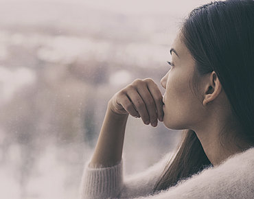 Junge Frau schaut traurig aus dem Fenster