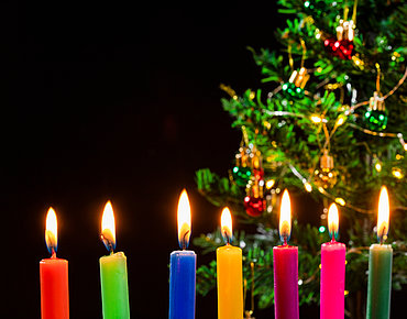 7 Leuchtende Kerzen mit Weihnachtsbaum im Hintergrund