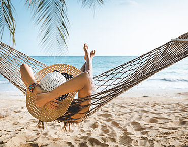 Symbolbild Urlaub: Frau liegt in Hängematte am Strand