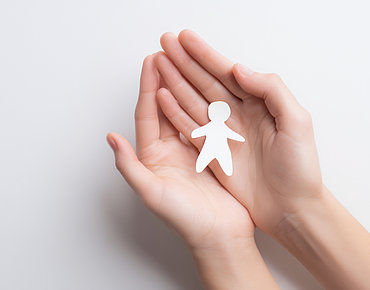 Symbolbild Fehlgeburt, ineinandergefaltete Hände mit Papiermänchen in der Mitte