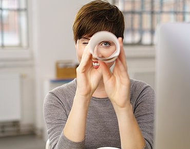 Frau schaut durch zusammengerolltes Papier
