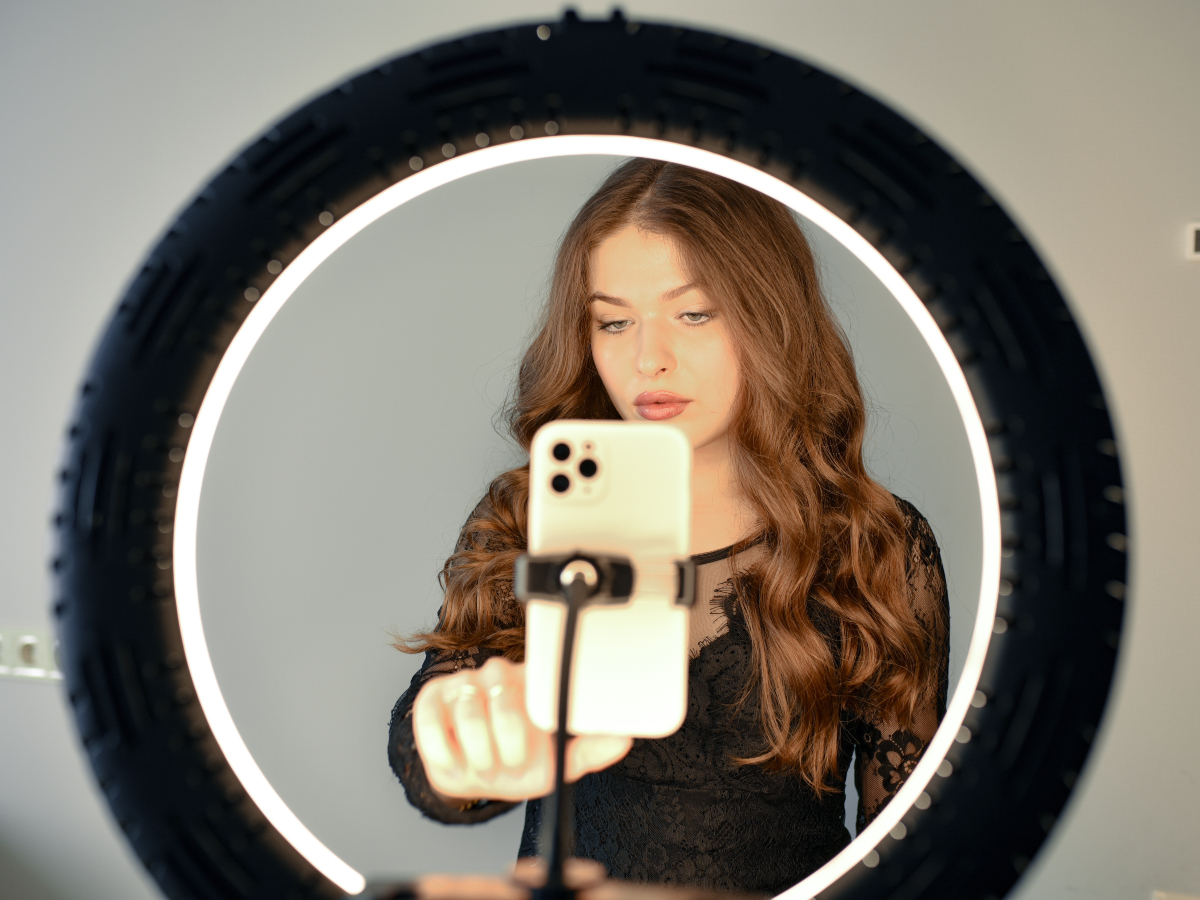Junge Frau filmt sich selbst mit einem Handy und Ringlicht Junge Frau filmt sich selbst mit einem Handy und Ringlicht