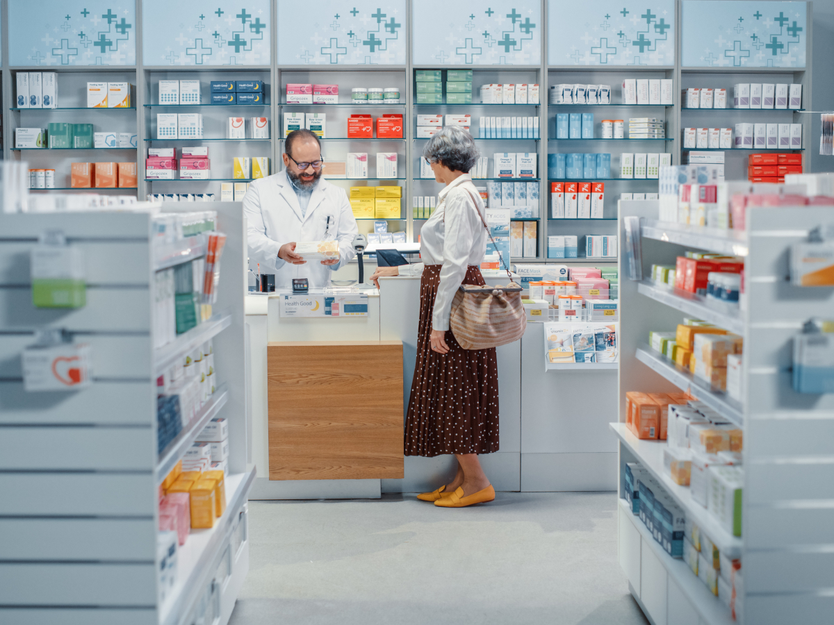 Frau steht an der Theke und redet mit dem Apotheker