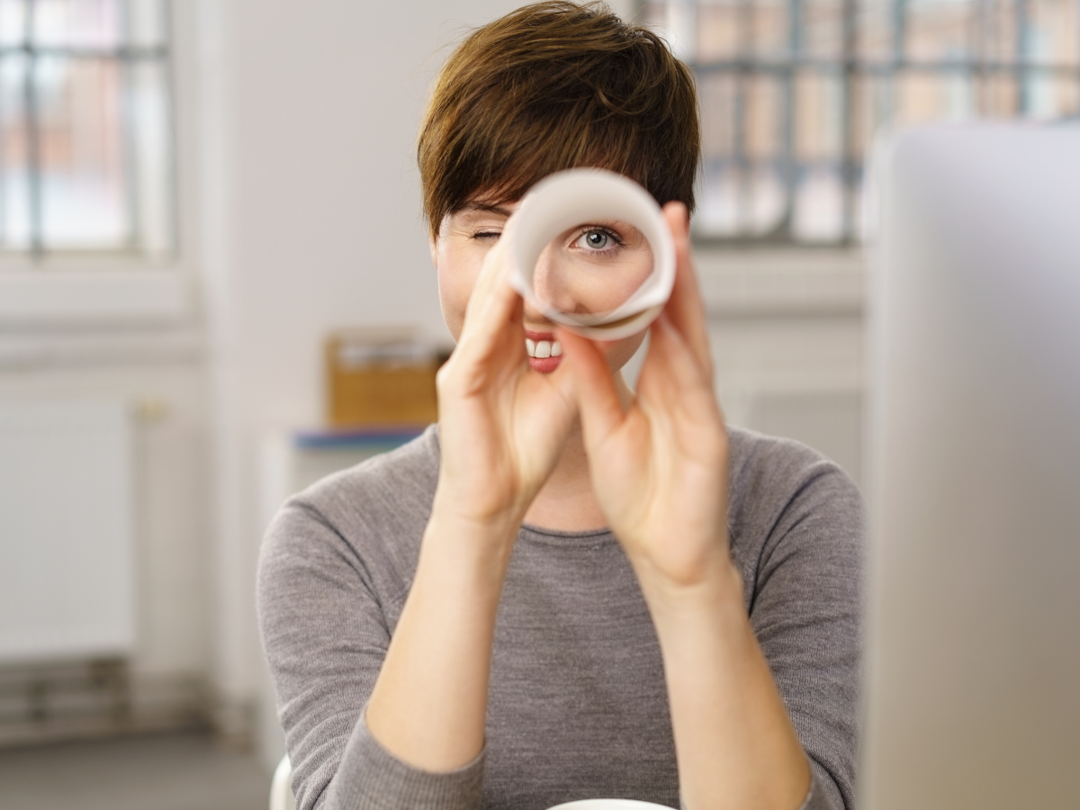 Frau schaut durch zusammengerolltes Papier