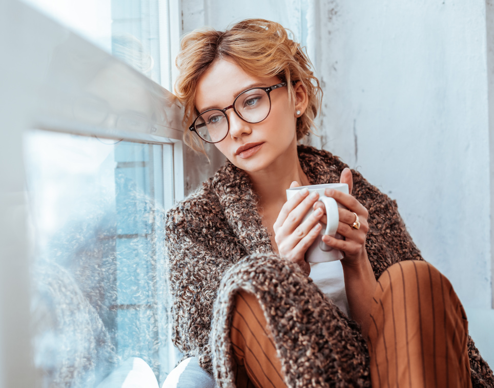 Mädchen sitzt am Fenster mit einer warmen Schokolade