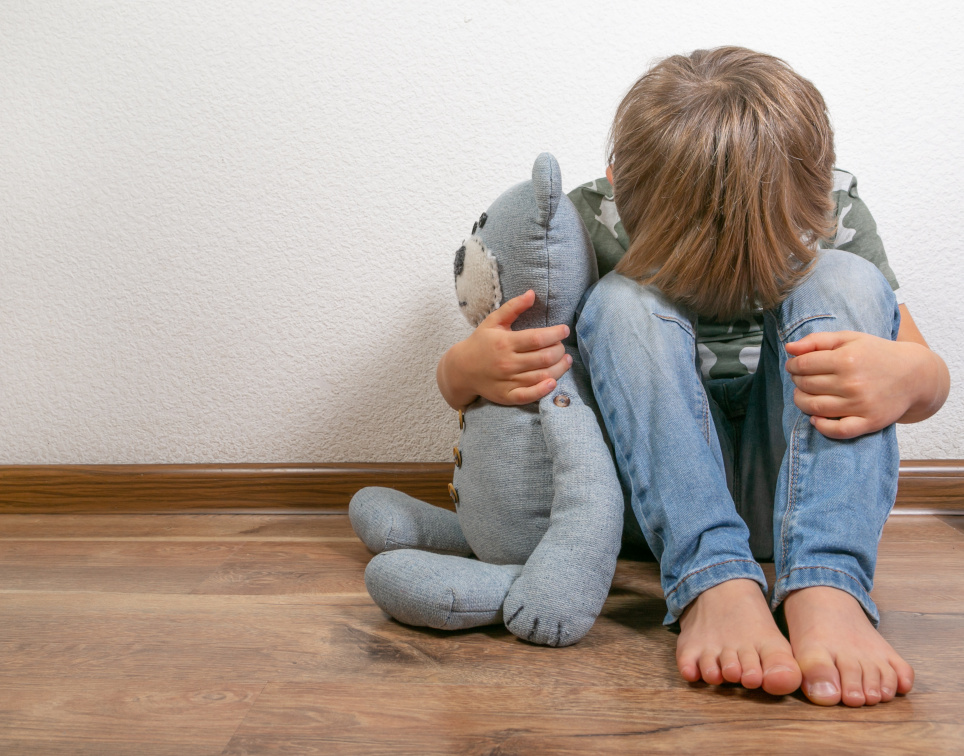 Kind sitzt verängstlich mit seinem Teddy an der Wand